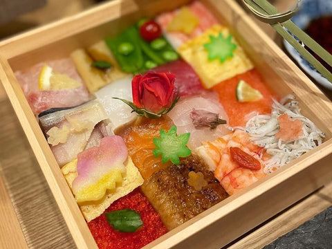 A box of hakozushi with different fish on each square and a flower shaped topping on each