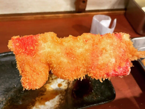 A stick of beni shoga tempura with a golden-brown crust and a pink hue underneath