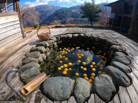 An outdoor bath filled with plenty of yuzu with a mountain view in the background