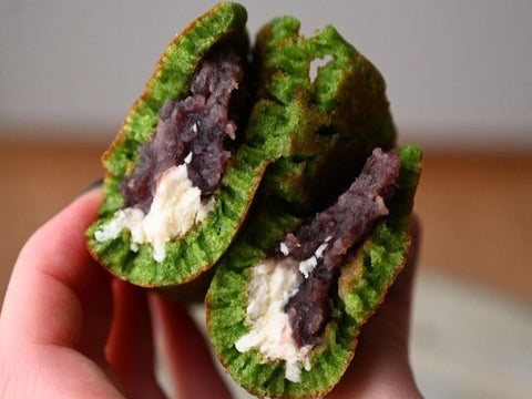 A folded green matcha dorayaki split in half showing an anko and butter cream filling