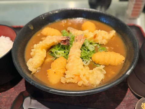 A bowl of udon with a curry broth and shrimp tempura and fried potato on top