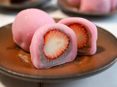 A plate of pink strawberry mochi dumplings with a strawberry in the center