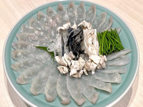 A plate of thinly sliced puffer fish on a blue plate with veggies and boiled puffer fish on top