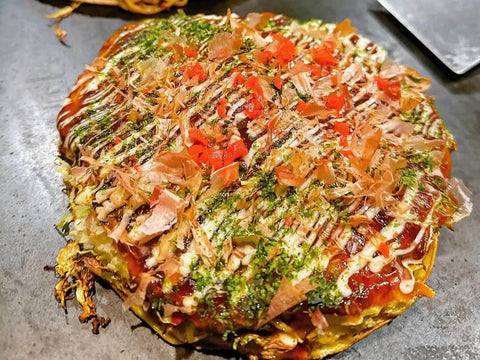 A thick okonomiyaki with a sauce, mayo, and beni shoga topping over yakisoba noodles