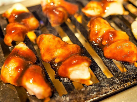 Glazed pieces of chicken cook over a yakiniku grill