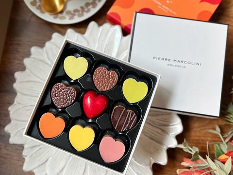 A box of nine heart shaped chocolates sits on a table