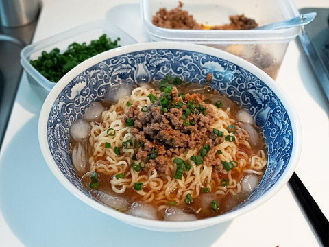 A bowl of ramen with ice in the soup and chives and ground beef on top