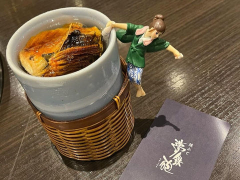 A cup of sake with grilled fish fins inside and a cup topper hanging off the side