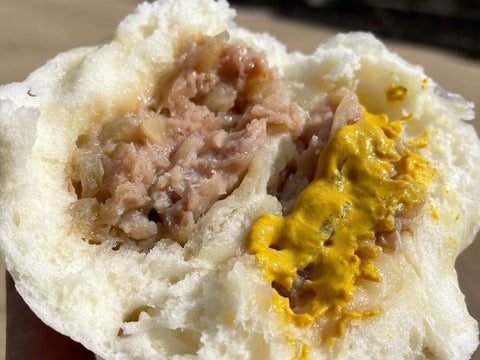 A nikuman pork bun split in half with mustard on one side