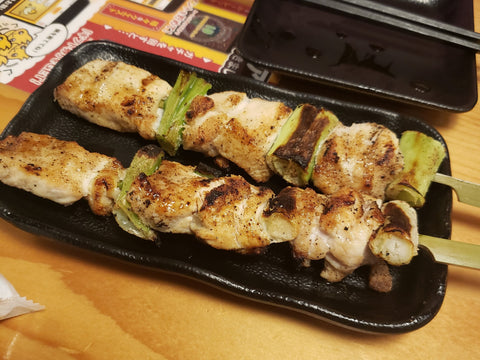 Two sticks of chicken skewered and grilled with green onion on a black plate