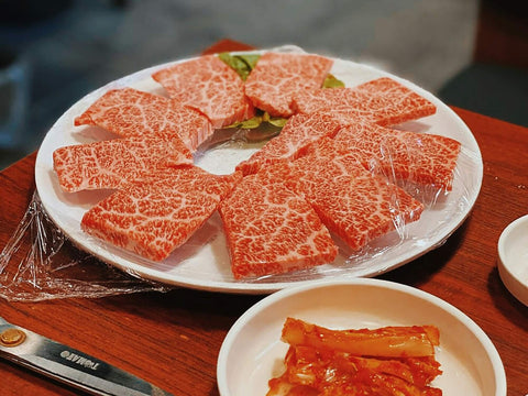 A plate of high-quality marbled wagyu sits in front of a dish of kimchi