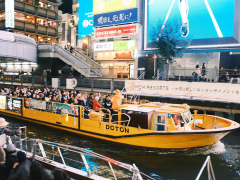 A boat of people on the Dotonbori Canal taking photos of Glico Man