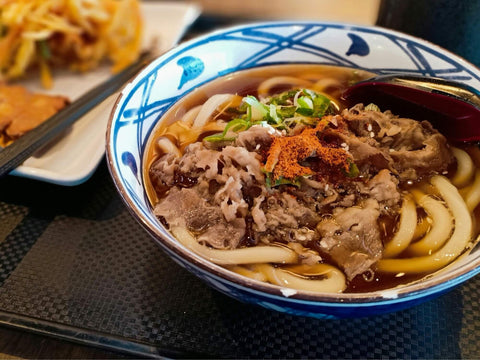 A bowl of udon with beef strips, green onion and chili pepper on top