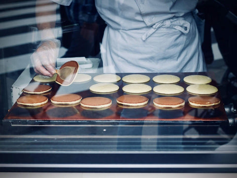 A griddle full of dorayaki being cooked with a worker flipping one