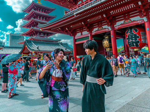 A Japanese man and woman in yukatas walk in front of a Japanese temple