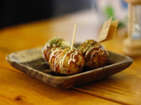 Three takoyaki balls sit on a plate with a toothpick sticking out