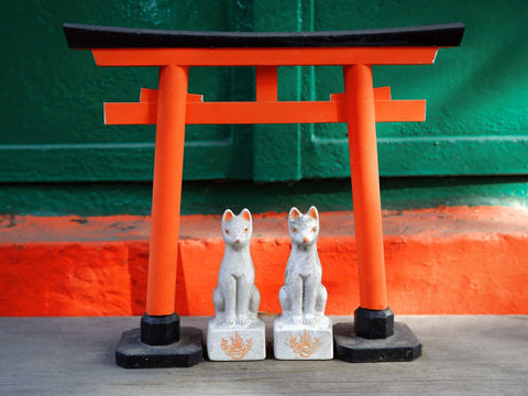 Two fox figurines sit in front of a Japanese torii gate