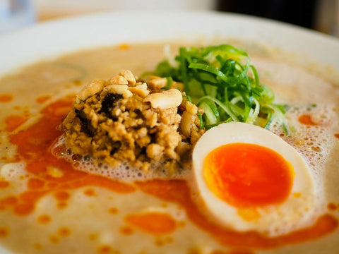 A bowl of tantanmen ramen with ground pork, egg, peanuts, and lots of chili oil on top