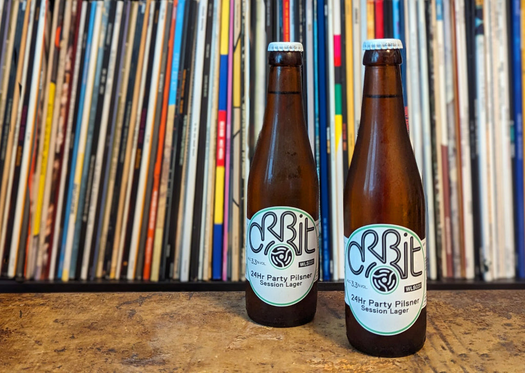 Two Party Pilsner beer bottles in front of stacked vinyl