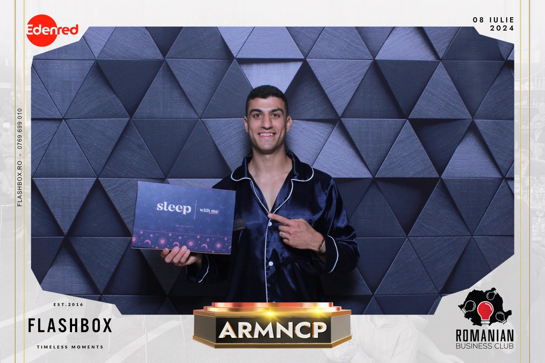 Man in dark pajamas holding a 'sleep with me' sign in front of geometric background.