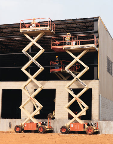 A couple of JLG all terrain scissor lifts extended next to a building forgoing construction.