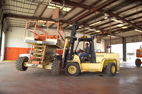 Image of service technician operating a industrial forklift to move a JLG scissor lift for service.