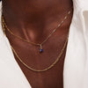 Person wearing a 14k gold Birthstone Charm necklace with a blue stone pendant.