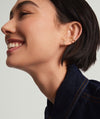 Woman smiling, showcasing Pavé Diamond X Studs in her ear. The 14k gold earrings feature responsibly sourced pavé diamonds in an elegant overlapping tubular design.