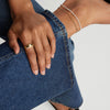 Micro Pearl Anklet: Close-up of a hand showcasing a handcrafted 14k gold anklet with freshwater pearls, worn stylishly over blue jeans.