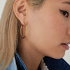 Close-up of a woman's ear wearing Tube Oversized Hoops with a clicker closure, highlighting their bold, lightweight design for comfort and security.