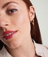 Close-up of a woman wearing a handcrafted 14k gold Single Patra Hoop Charm in her ear.