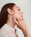 A woman with red hair wears a handcrafted 14k gold Patra Ring and matching gold earrings, with her hand gently touching her face.