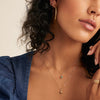 A woman wearing the Birthstone Sphere Charm necklace with matching earrings, showcasing the blue sapphire set in 14k solid gold.