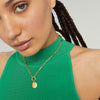 Woman wearing a green top and a gold Engravable Disc Charm necklace, showcasing a sophisticated fashion accessory.