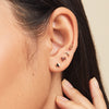 Close-up of a woman's ear wearing the Moon Flat Back Stud, featuring a small gold crescent moon design with a comfortable threadless flat back.