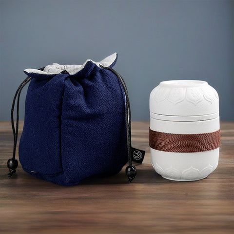 A white portable teapot with a copper band next to a blue fabric drawstring bag on a wooden surface.