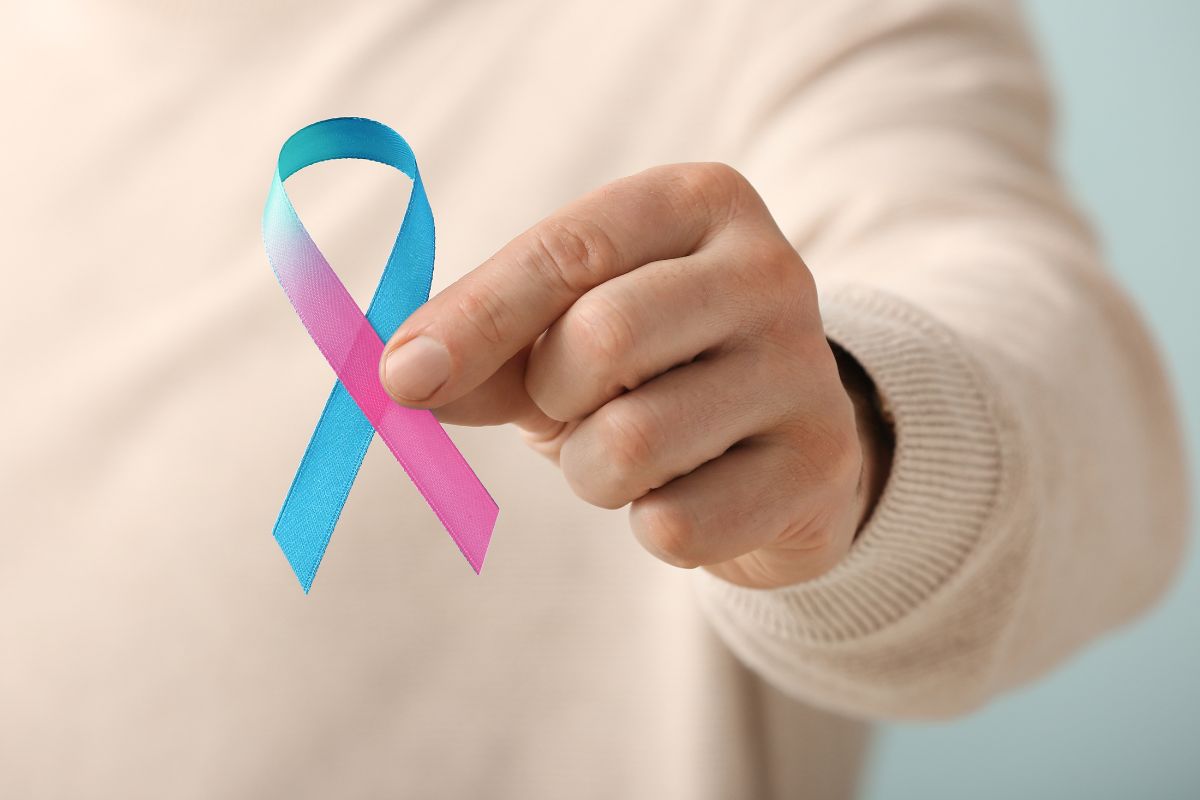 A person holding pink and blue ribbon for infertility awareness.