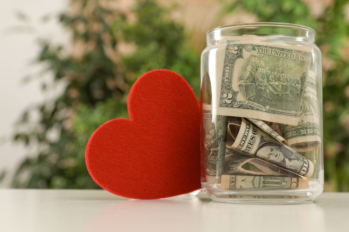 A small jar of money kept for donation and a red heart behind it.