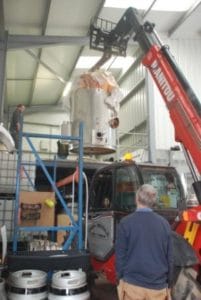 An image of an alcohol still being lifted into place in a warehouse as a man looks on