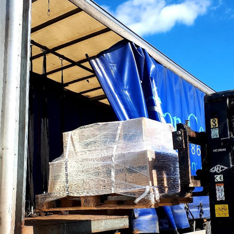 A picture of a pallet of henstone boxes being lifted off a truck by a forklift