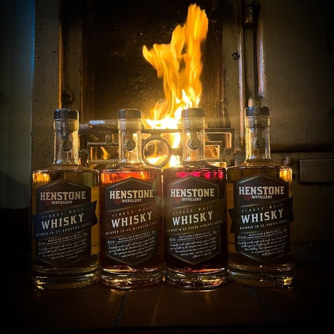 A picture of 4 bottles of henstone whiskey in front of a log burning fire