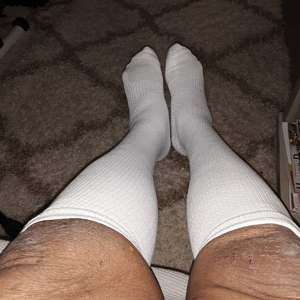 Person wearing white compression socks, seated on a textured rug.