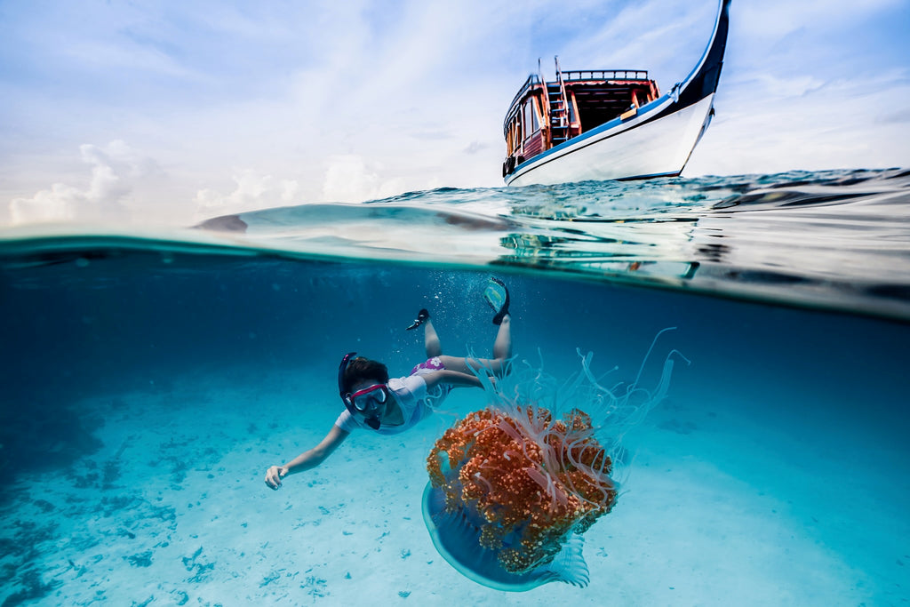 Split level half over half underwater photo of a swimmer with jelly fish and boat in the background