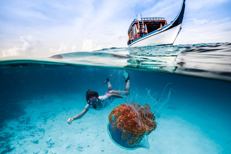 Imagem subaquática de nível dividido meio a meio usando a porta de cúpula telefônica subaquática Outex mostrando água-viva, mulher e barco no oceano