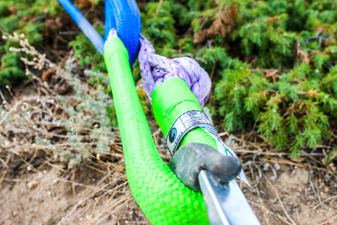 An off-road vehicle in rugged terrain, successfully using a Ravenox soft shackle for a recovery operation. The shackle, made of strong synthetic fibers, is visibly attached to the vehicle, demonstrating its lightweight yet durable nature, crucial for such challenging outdoor activities.