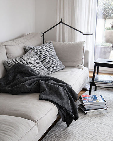 cremefarbenes Sofa mit grauen Kissen und dunkelgrauer Wolldecke