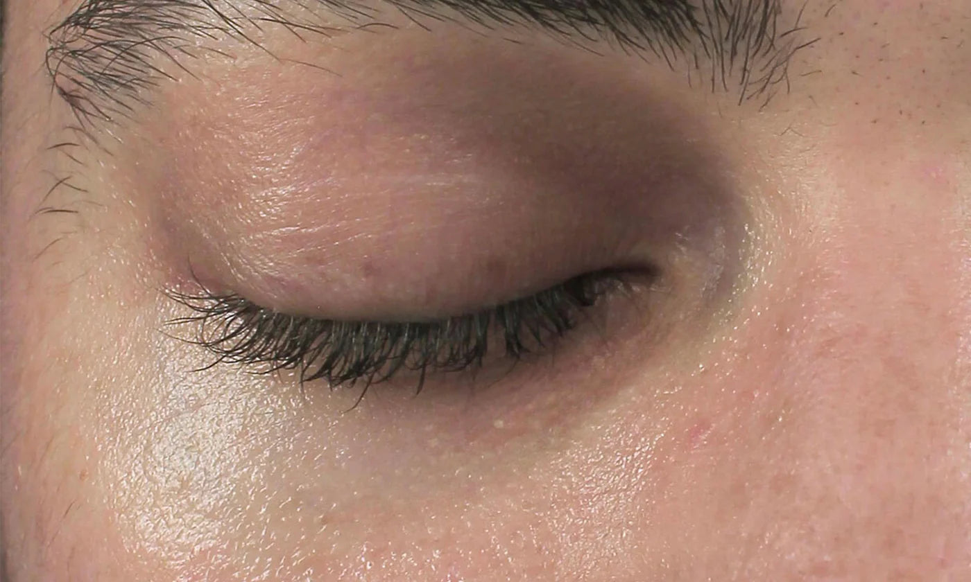 Close-up of a person's closed eye with lashes and eyebrows visible.