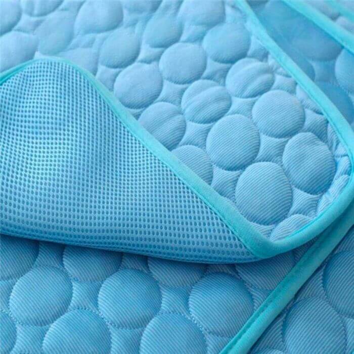Detalhe próximo de um tapete de resfriamento para pets na cor azul claro, mostrando a textura e a borda do tecido respirável. O design é composto por círculos em relevo que ajudam na circulação do ar e na dissipação do calor.