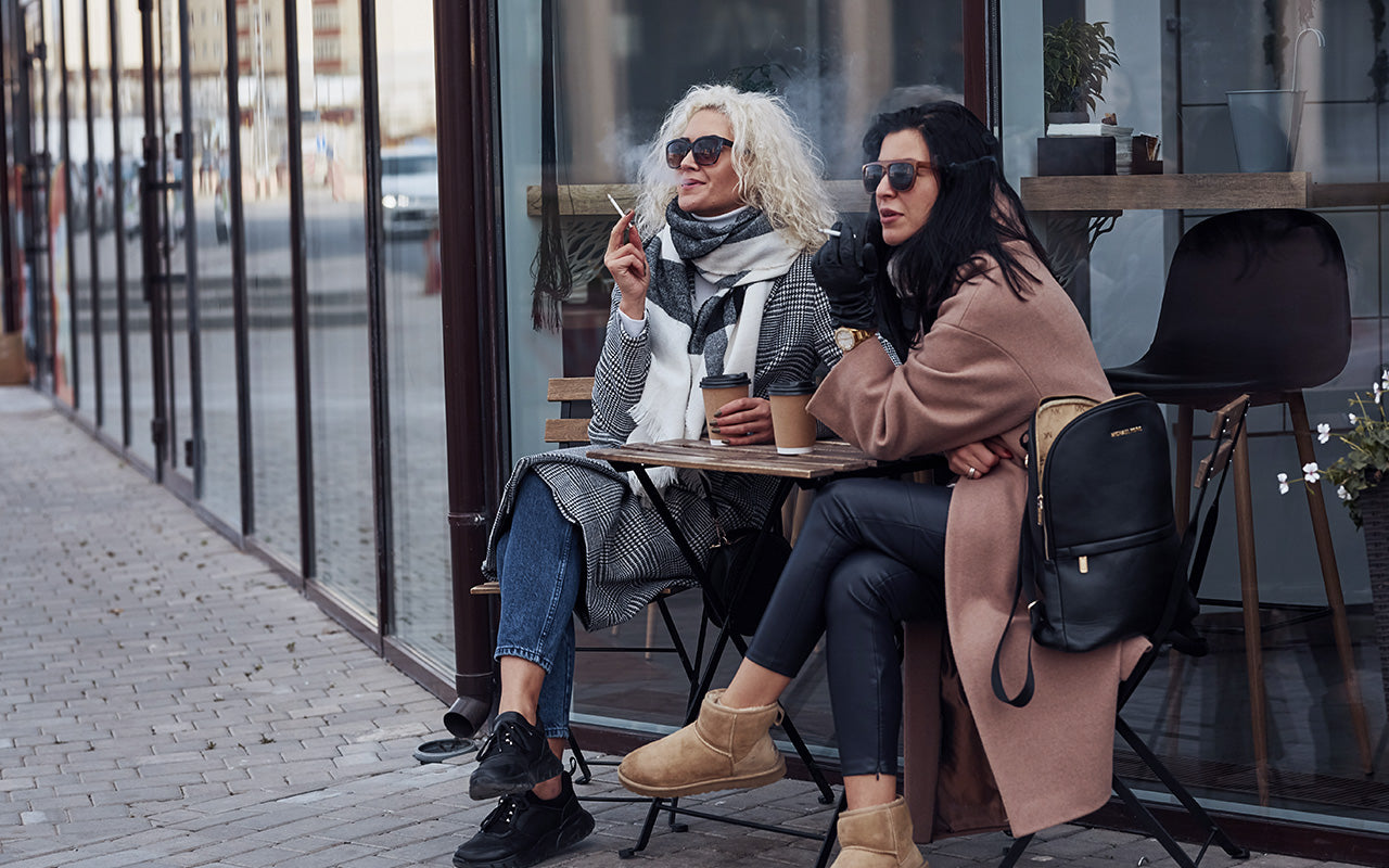 Two women sat outside on chairs smoking cigarettes