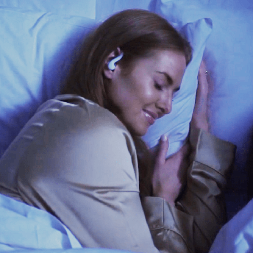 Close up of woman sleeping on side, smiling and fast asleep wearing SoundOff Sleep earbuds.